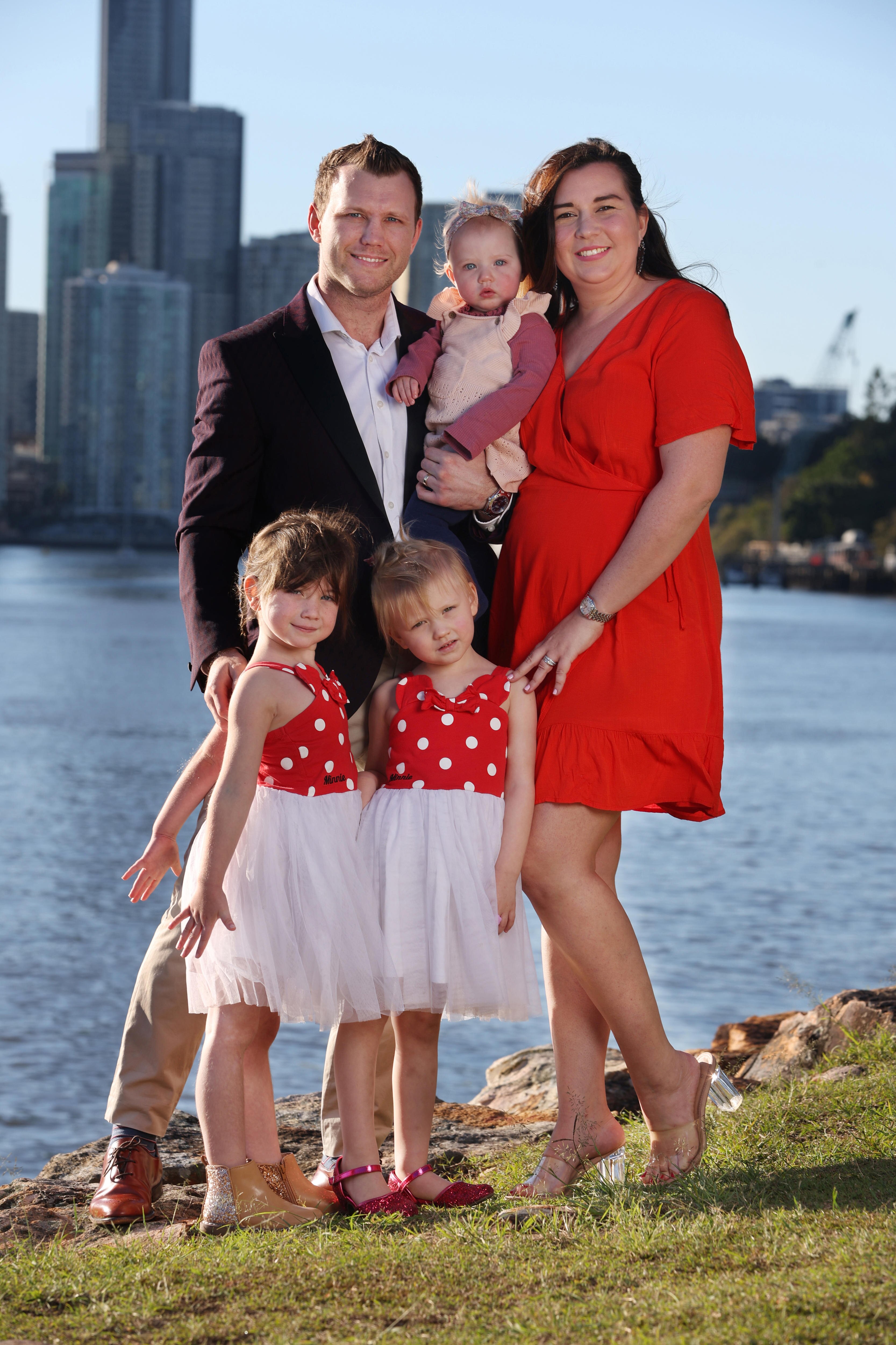 Husband and wife stand with three three young girls to take a photo