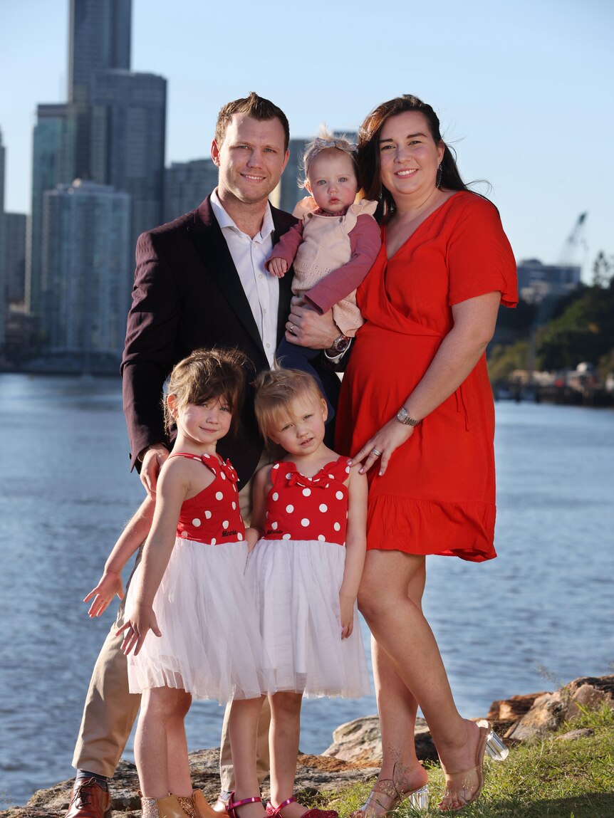 Husband and wife stand with three three young girls to take a photo