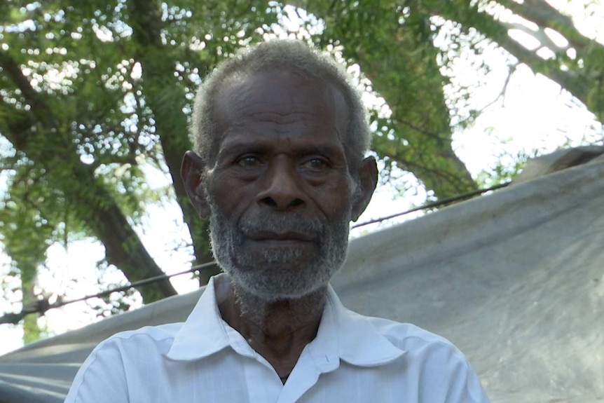 A man looks at the camera and stands in front of a tree.