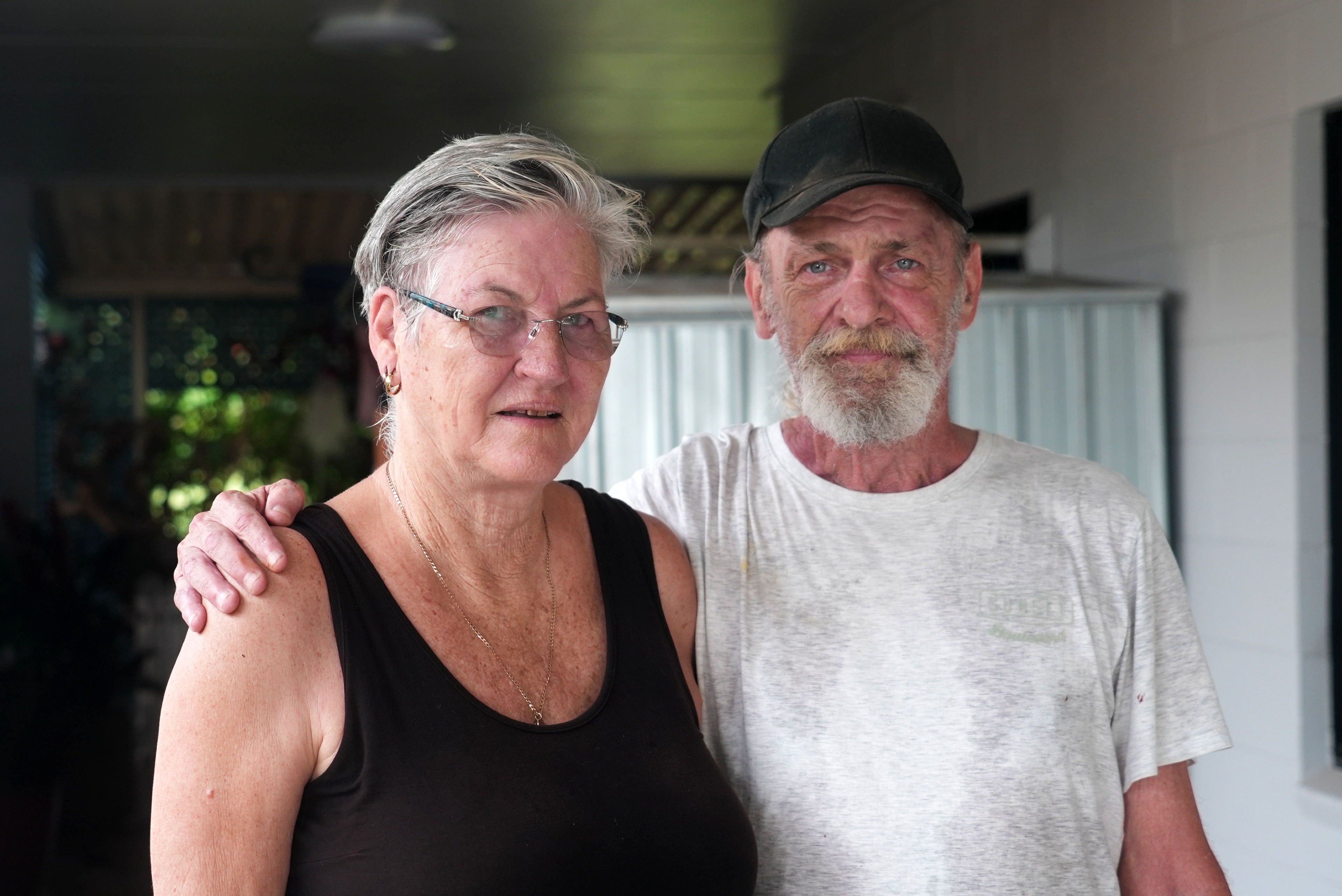 A man stands with his arm around a woman, both looking at the camera