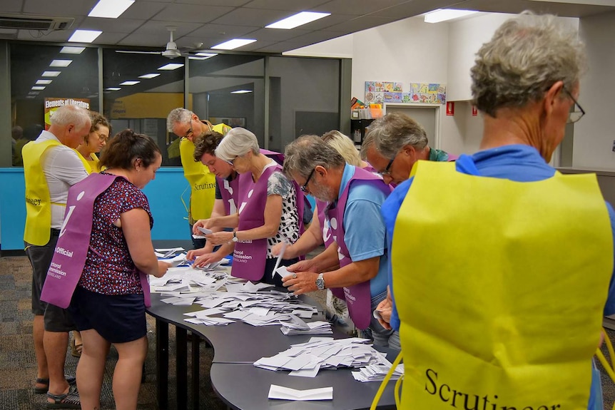People in purple and yellow smocks count votes on a table.