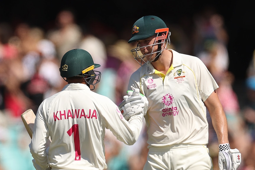 Cameron Green shakes the hand of Usman Khawaja, both wearing batting kit