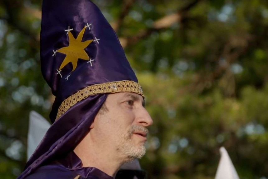 A man wearing a purple pointy hat, with the photo taken from the side.