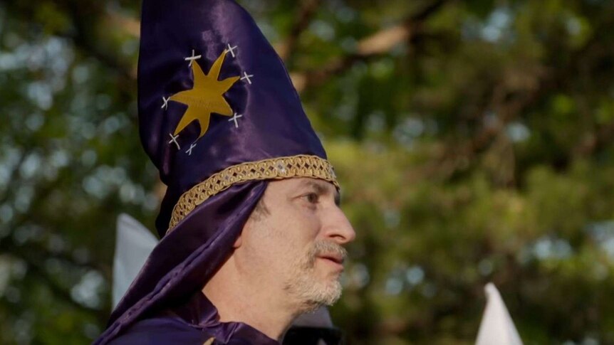 A man wearing a purple pointy hat, with the photo taken from the side.