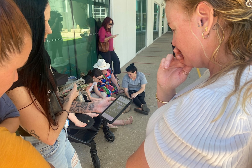 Women affected by the care at the Mackay Hospital watch the findings on their phones.