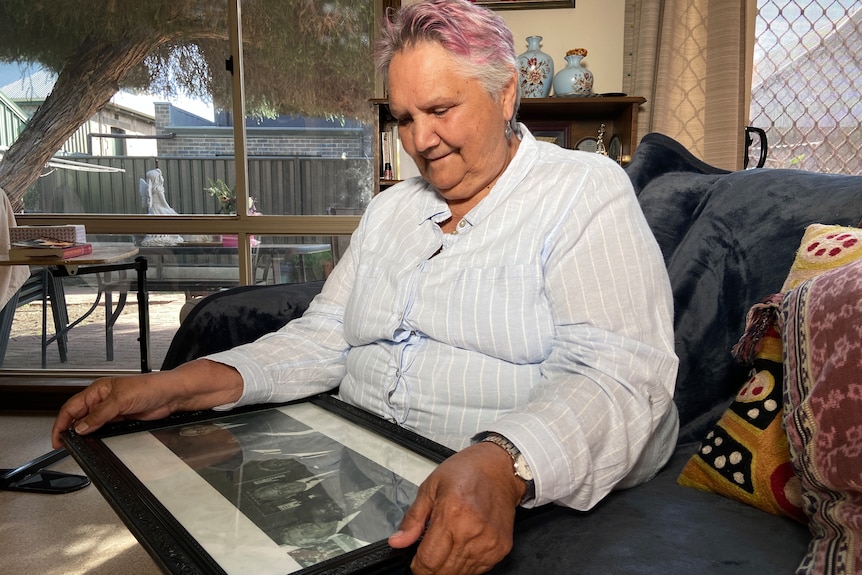 A seated woman smiles as she looks at a photo she holds on her lap