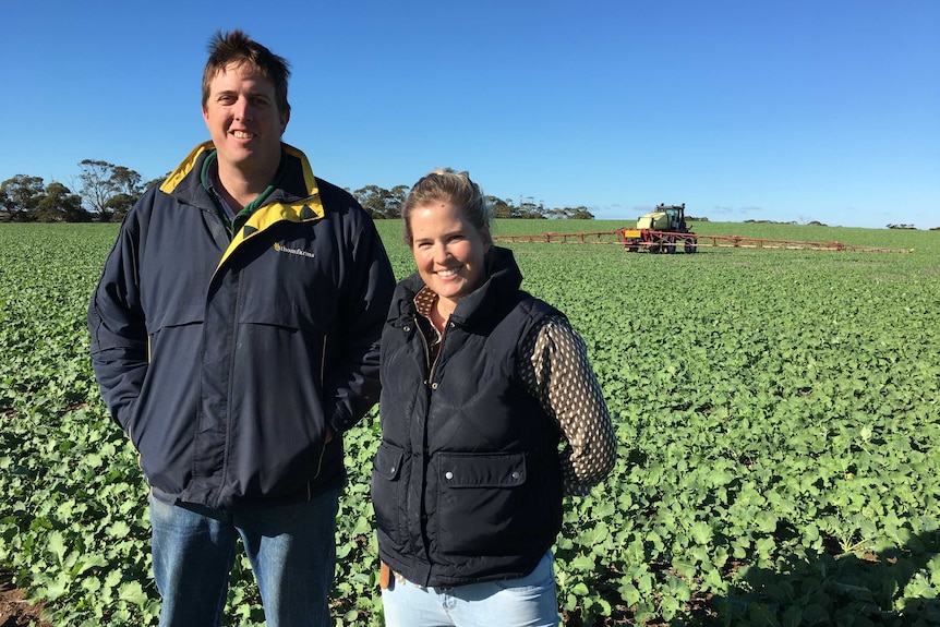 Man and woman stand in front of herbicide tractor in canola field.