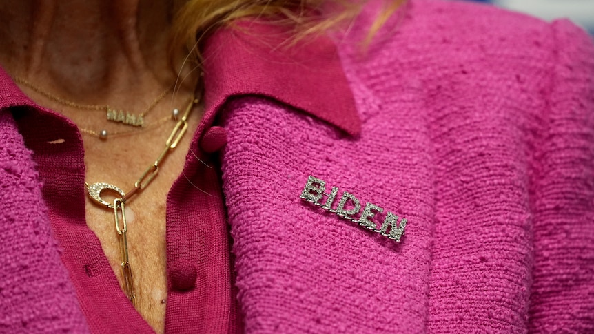 Jill Biden wears a pink suit with a pin that says BIDEN on the collar.