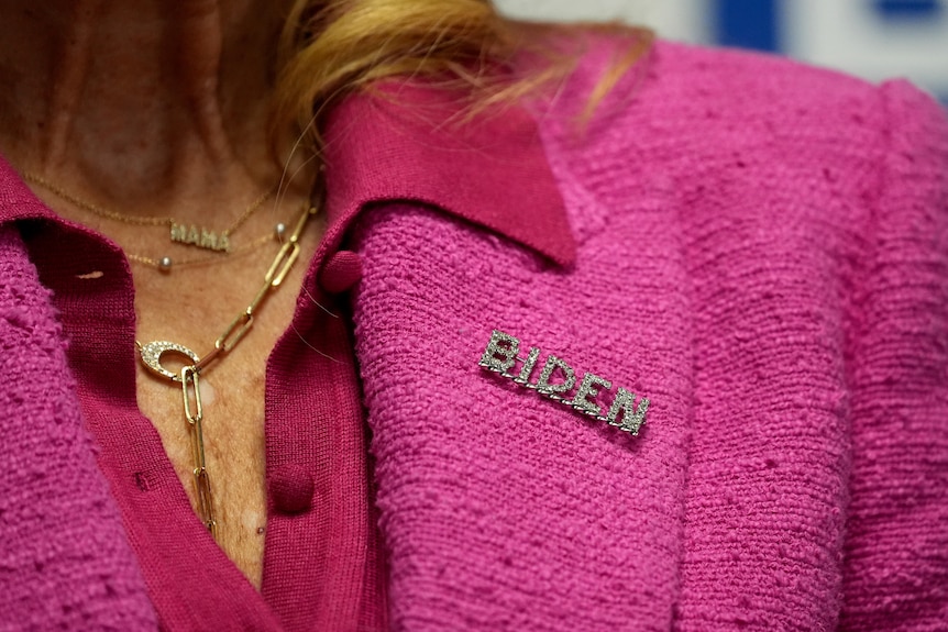 Jill Biden wears a pink suit with a pin that says BIDEN on the collar.