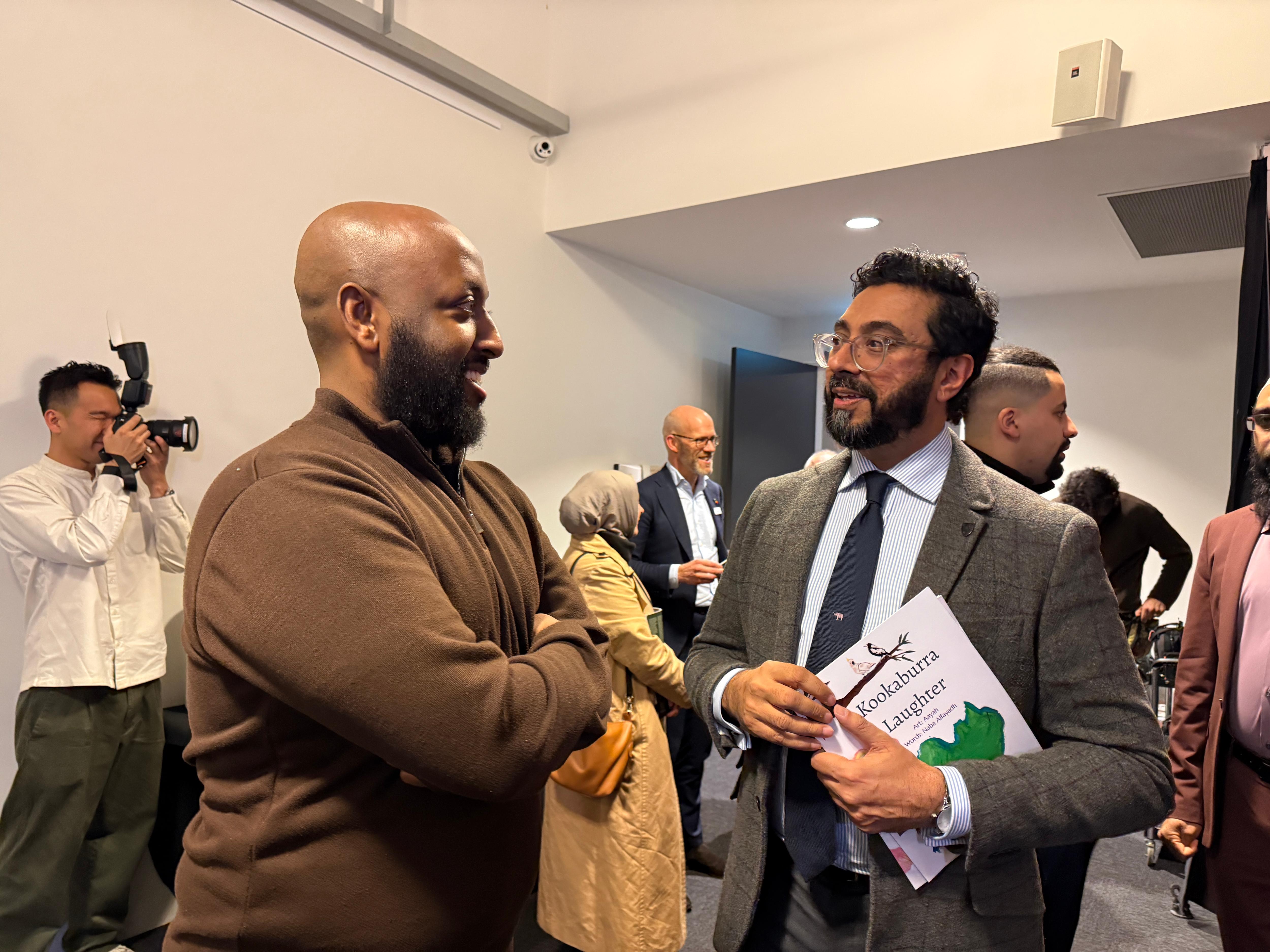 Two middle aged Middle Eastern men stand and talk in a room
