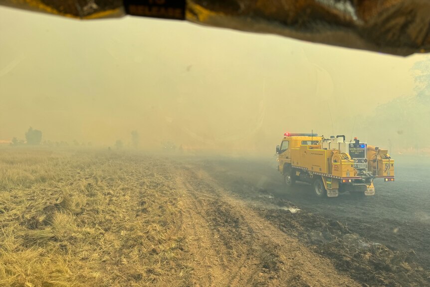 A firetruck travelling through smoke haze along burned ground