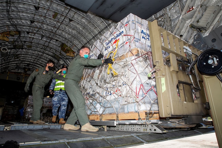 Australian Defence Forces members unload humanitarian assistance and engineering equipment from an aircraft.