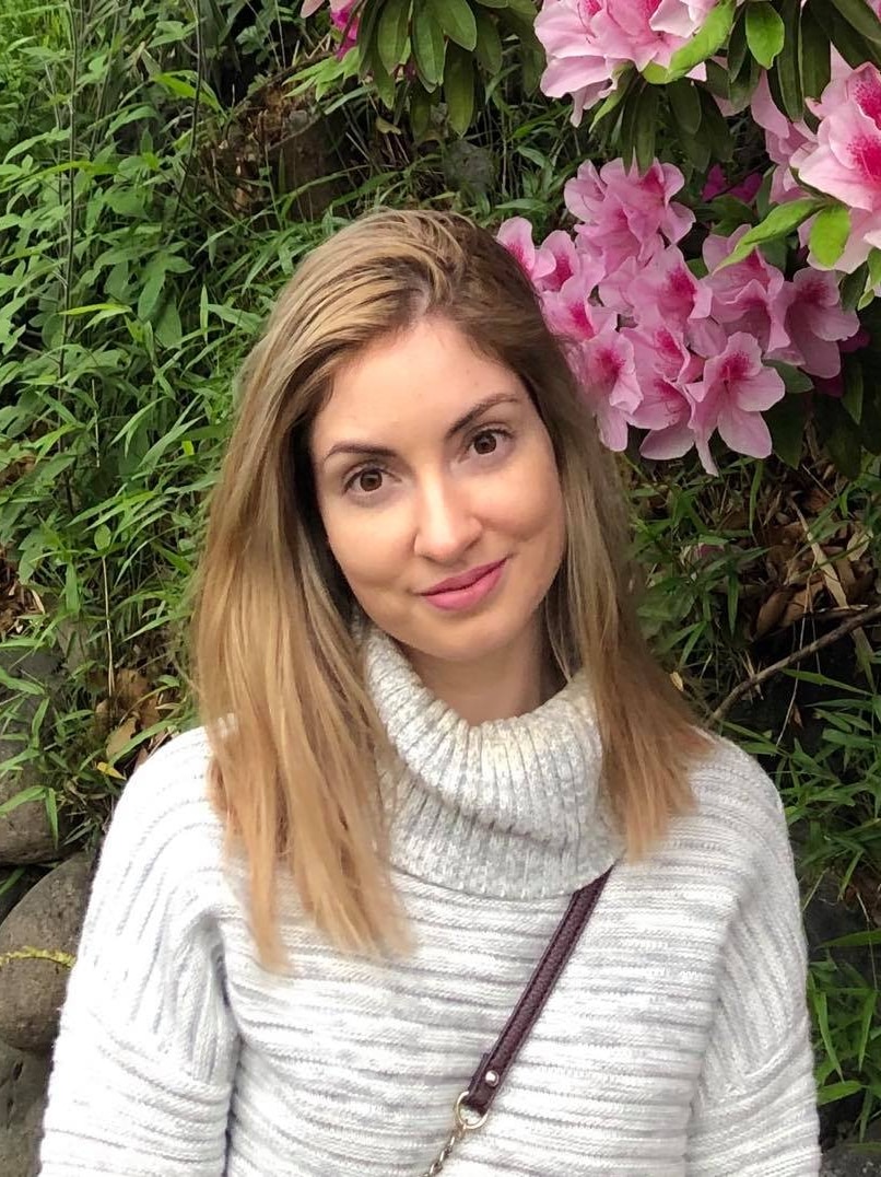 A woman smiles while standing under a flowering tree.