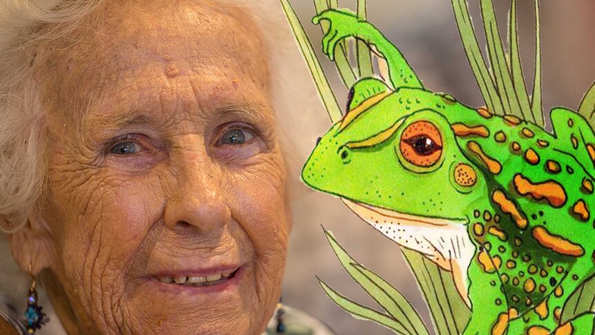 an older woman smiles at the camera while a drawing of a frog pokes out of some grass
