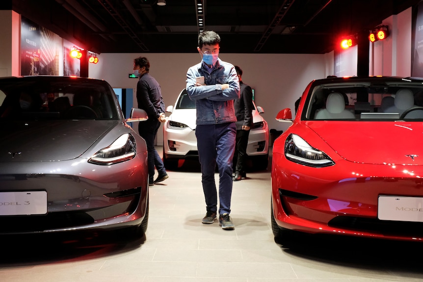 Un bărbat trece pe lângă sedanurile Tesla Model 3 și un SUV Tesla Model X la noul showroom Tesla din Shanghai