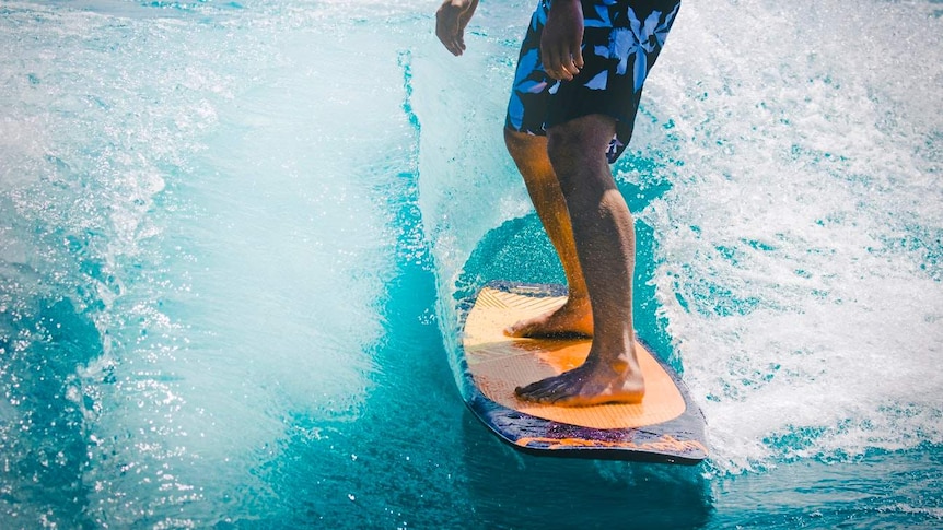 A man rides a wave on a long orange and purple surfboard to depict how to choose your first surfboard.