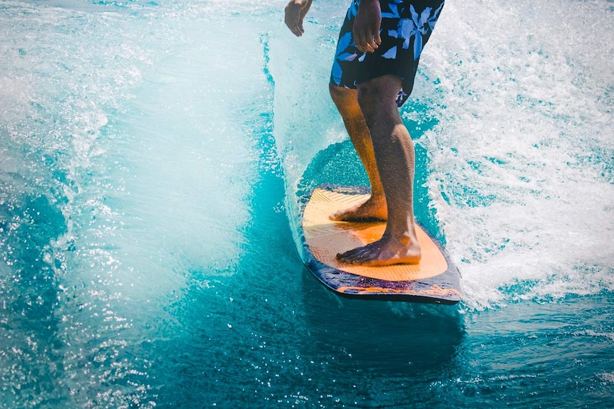 A man rides a wave on a long orange and purple surfboard to depict how to choose your first surfboard.