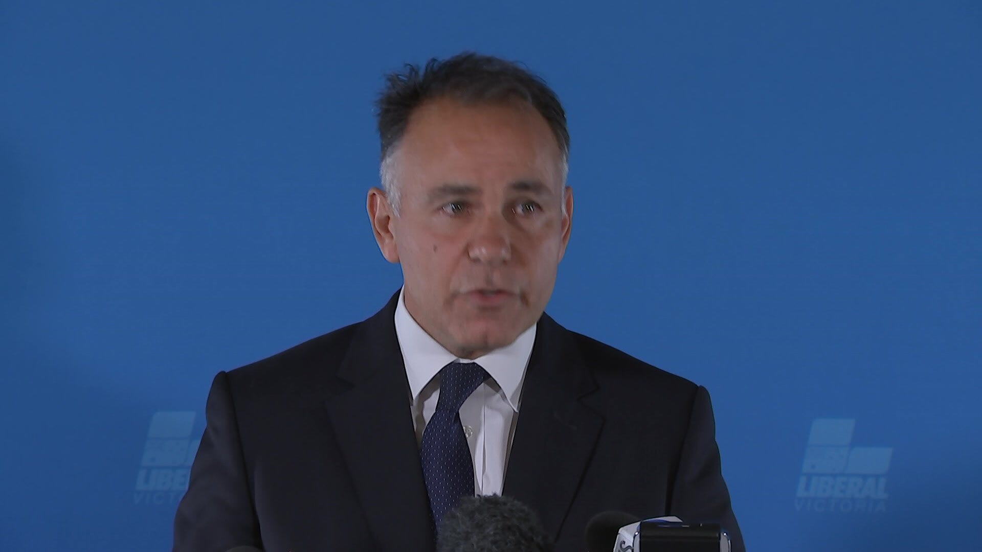 John Pesutto standing in front of a blue backdrop.