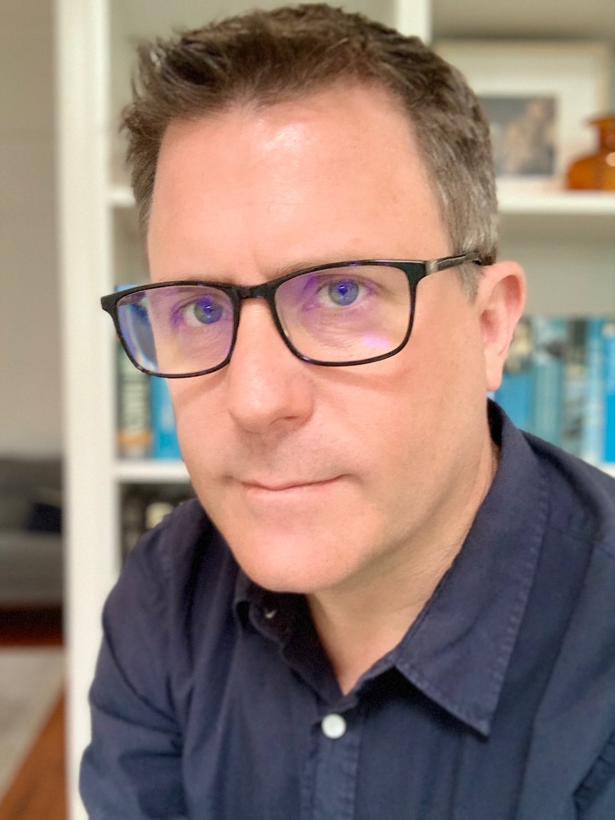 A man with glasses in front of a book shelf