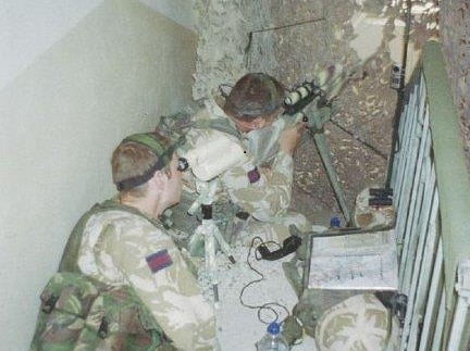 two men in camouflage shooting out of a window.