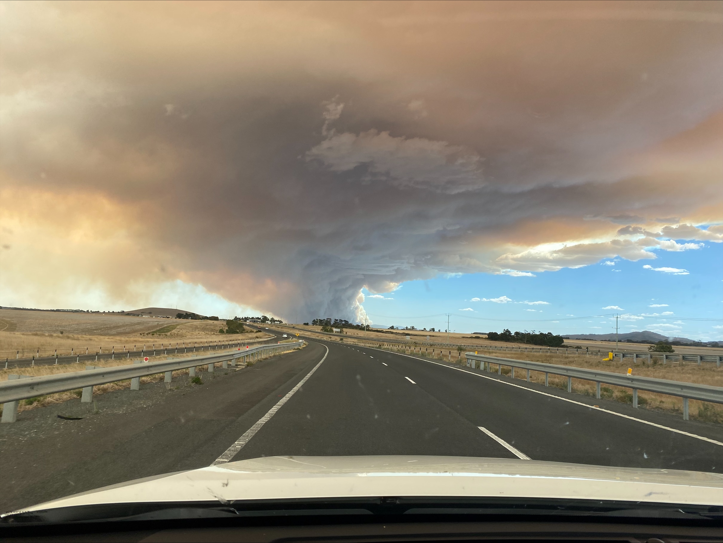 Smoke in the shape of a tornado forming near a road. 