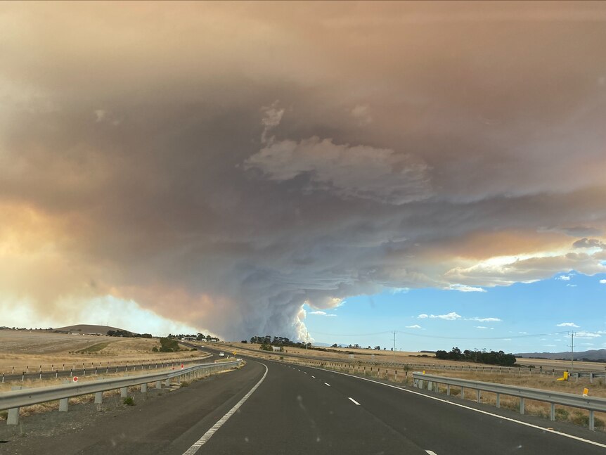 Smoke in the shape of a tornado forming near a road. 