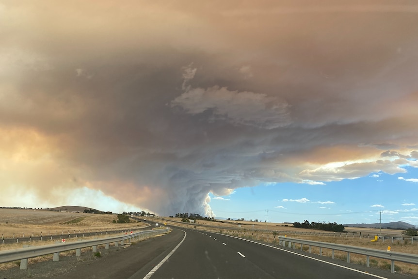 Smoke in the shape of a tornado forming near a road. 