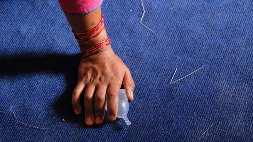 The hand of a woman decorated with bracelets grabs a Menstruation cup.
