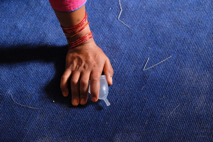 The hand of a woman decorated with bracelets grabs a Menstruation cup.