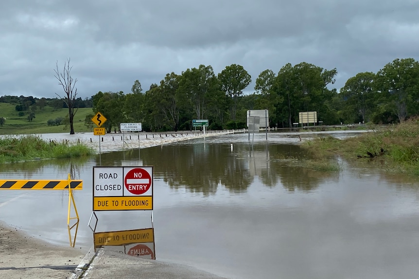 A swollen Teviot Brook closes Boonah Beaudesert Road at Coulson, with a 'road closed' sign in forefront.