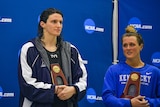 Two women hold trophies while standing in front of a blue backdrop