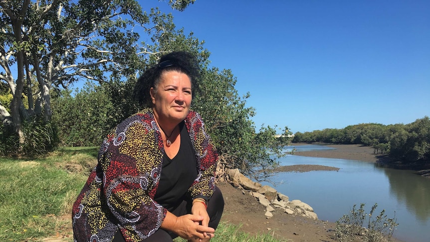 A woman kneels in front of a river