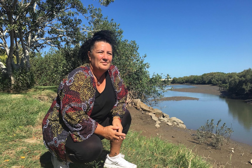 A woman kneels in front of a river