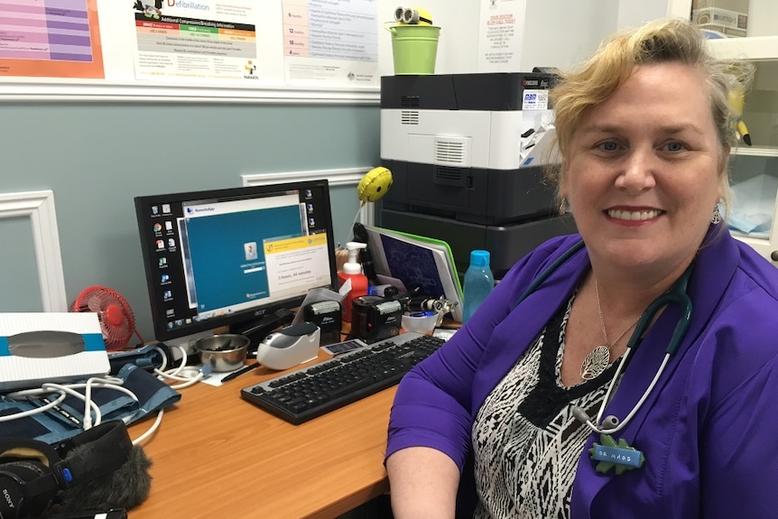 A doctor at her desk sitting in front of her computer with a stethoscope resting on her shoulders