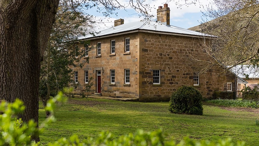 A large, double storey sandstone home, surrounded by trees.