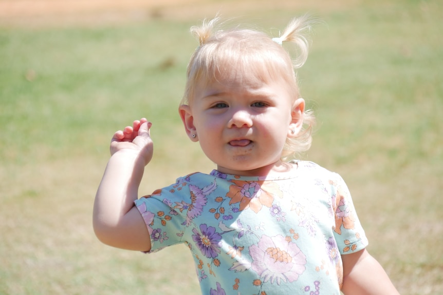 Baby girl runs toward the camera on grass.