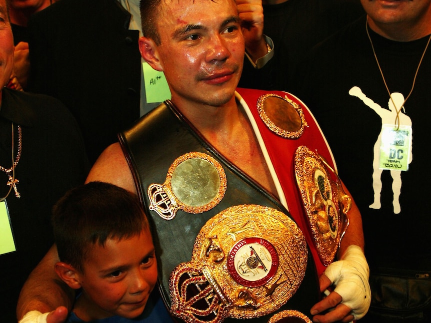 Kostya Tszyu holds belts and hugs Tim Tszyu