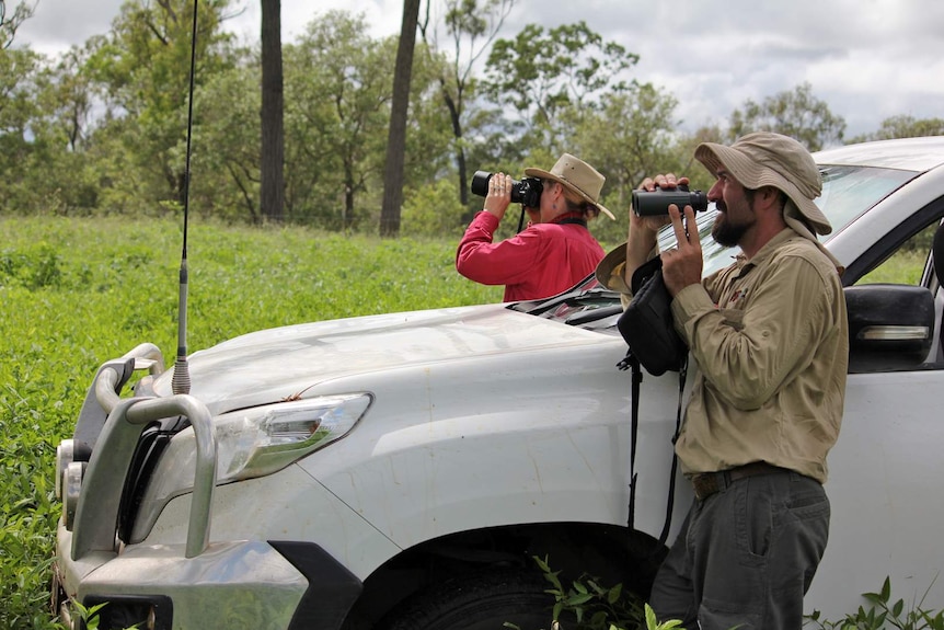 Two scientists look at a bird using a camera and binoculars