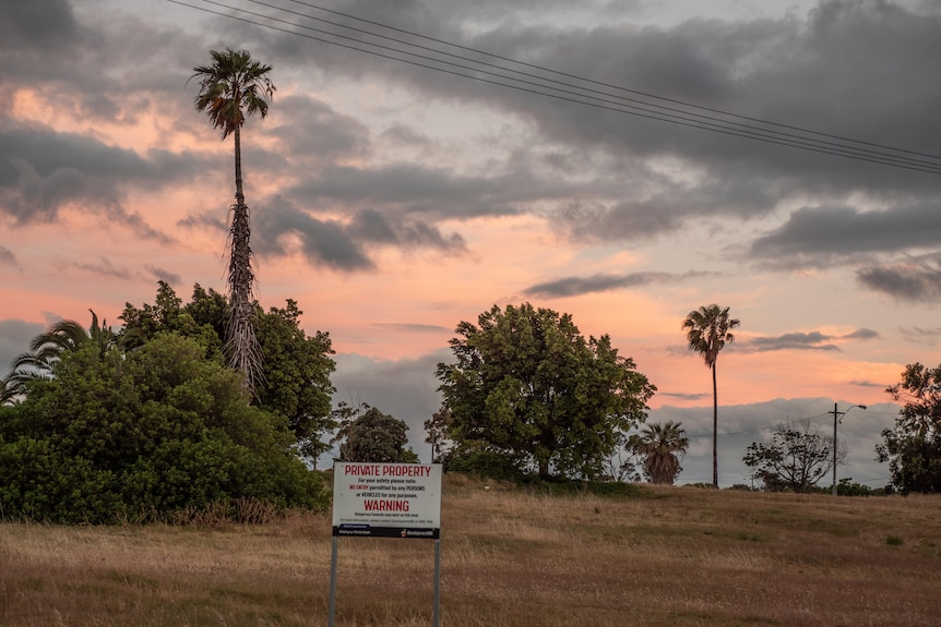 A vacant lot with a private land sign and a pink sunset