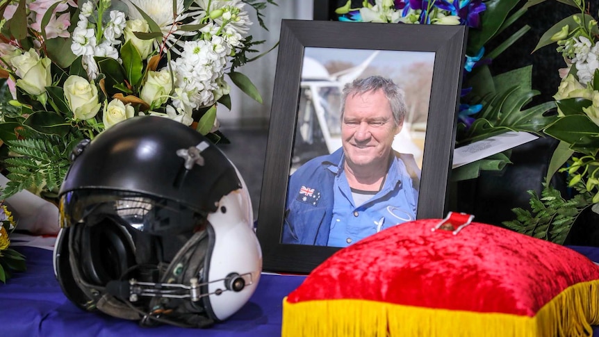 A photograph of a man next to flowers and a helmet.