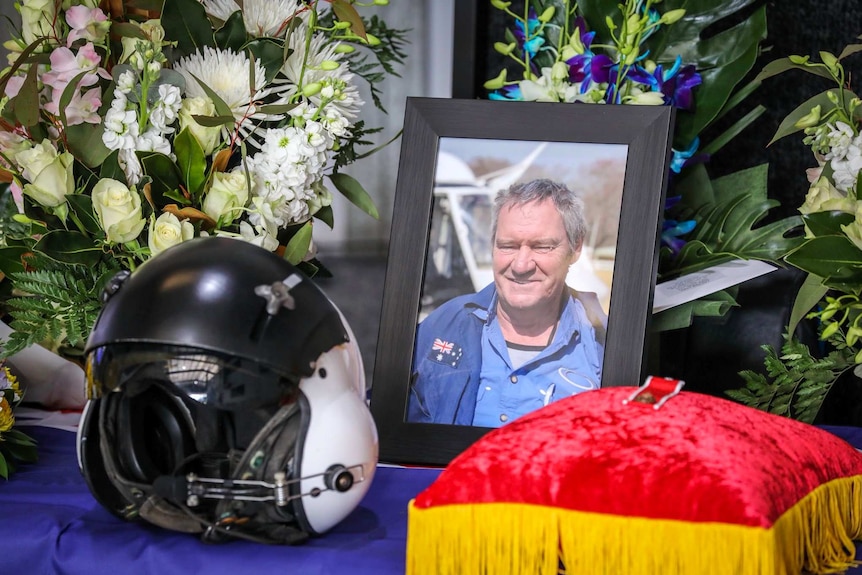 A photograph of a man next to flowers and a helmet.