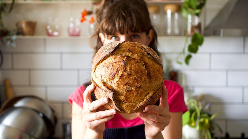 Woman holds a freshly baked sourdough loaf in her Adelaide kitchen, making sourdough at home.