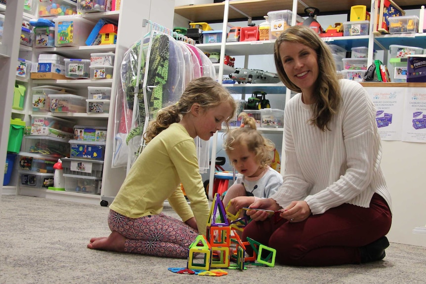 Woman plays with two children on the floor with toys.