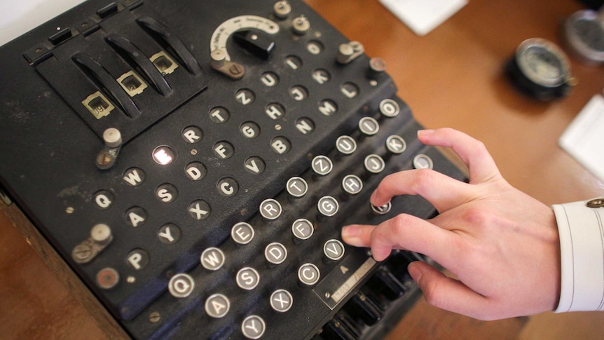 A hand pushes a key on the keyboard of a cipher machine