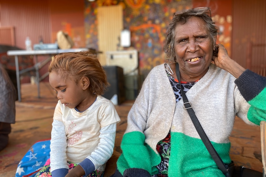 A woman smiles at the camera beside a child looking away 