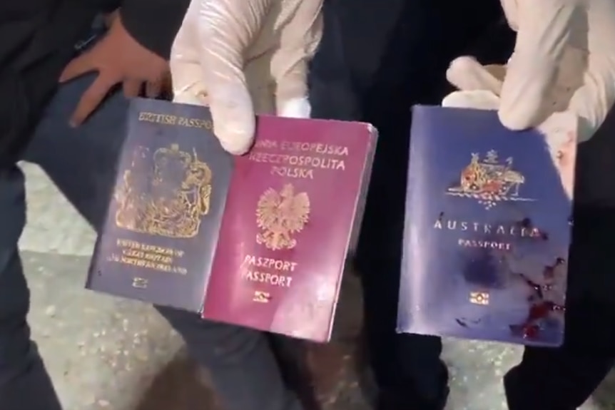 A person wearing gloves holds out a British, Polish and Australian passport with blood on them