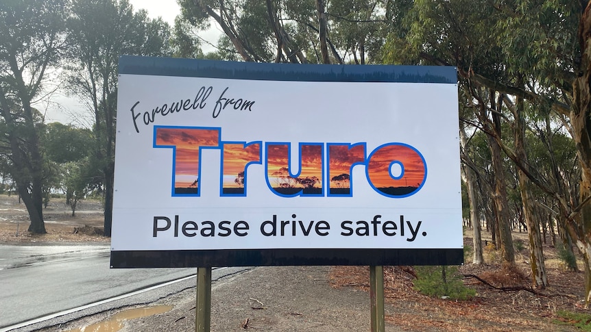 A white sign saying farewell from Truro in front of a wet road.