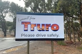 A white sign saying farewell from Truro in front of a wet road.
