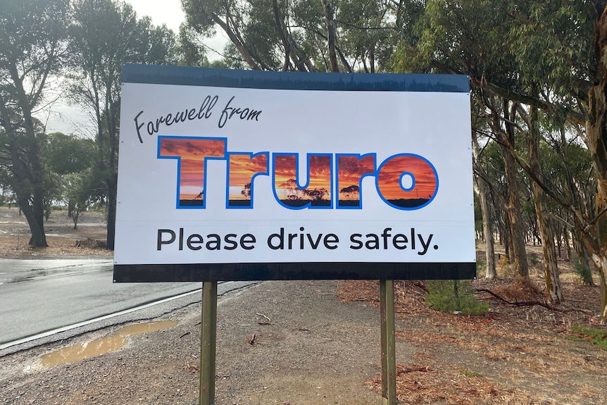 A white sign saying farewell from Truro in front of a wet road.