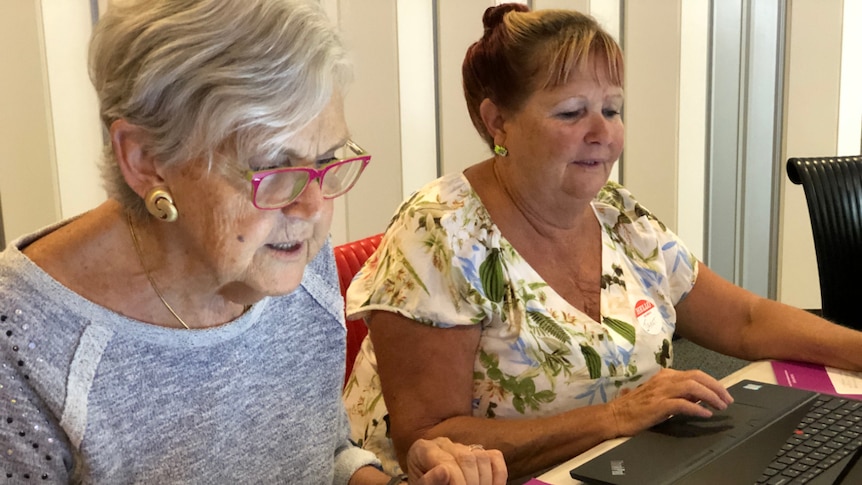 Two older women sitting in front of laptops, focussing on the computer screen.